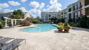 A swimming pool surrounded by lounge chairs and potted plants, with multi-story buildings in the background.