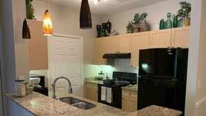 A kitchen with granite countertops, a stainless steel sink, a black refrigerator, and wooden cabinets.