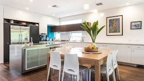 Una cucina moderna con isola centrale, mobili bianchi e zona pranzo con sedie bianche.
