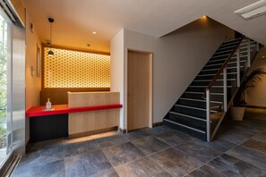 Een modern receptiegebied met een rode balie, een houten receptie bureau, een behang met patroon en een trap met een metalen leuning.