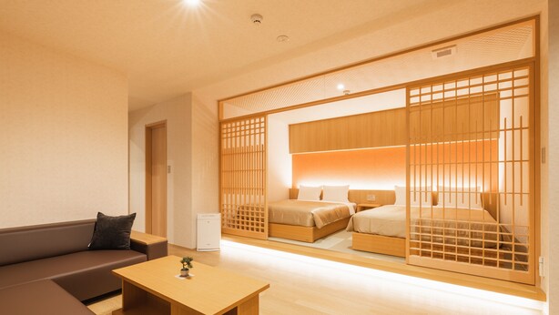 Een moderne hotelkamer met een bank, een houten salontafel, een bed met een houten hoofdeinde en een schuifdeur met een houten lattenwerkontwerp.