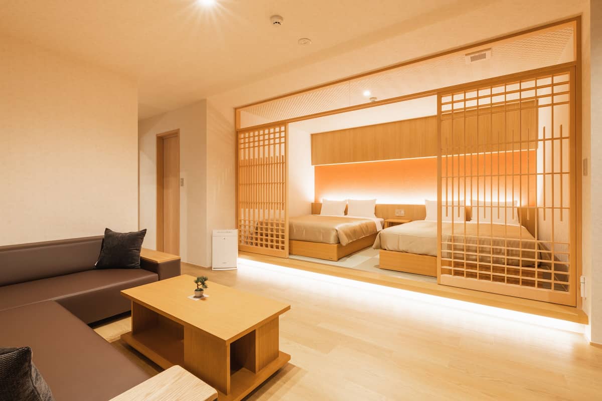 Une chambre d’hôtel moderne comprenant un canapé, une table basse en bois, un lit avec une tête de lit en bois et une porte coulissante ornée d’un motif en treillis de bois.