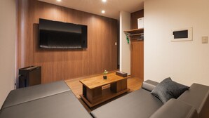Een moderne woonkamer met een flatscreen televisie aan de muur, een houten salontafel, een bank en een klein bijzettafeltje.