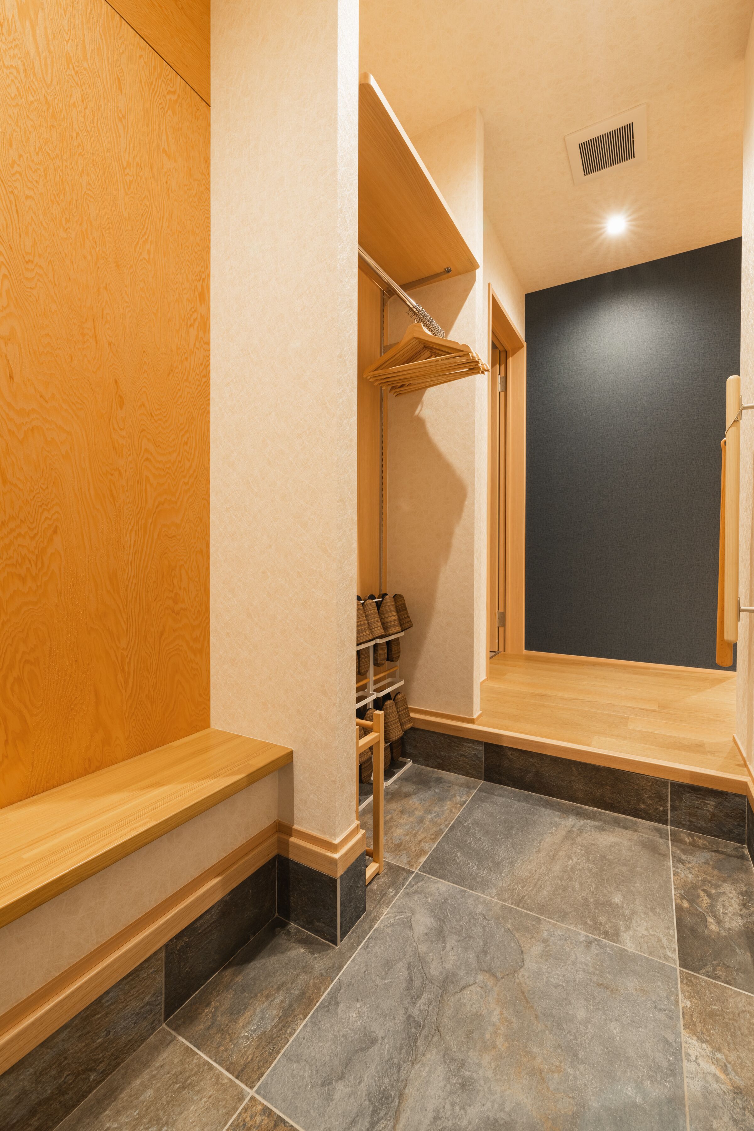 Un baño con banco de madera, suelo de baldosas y pared oscura.