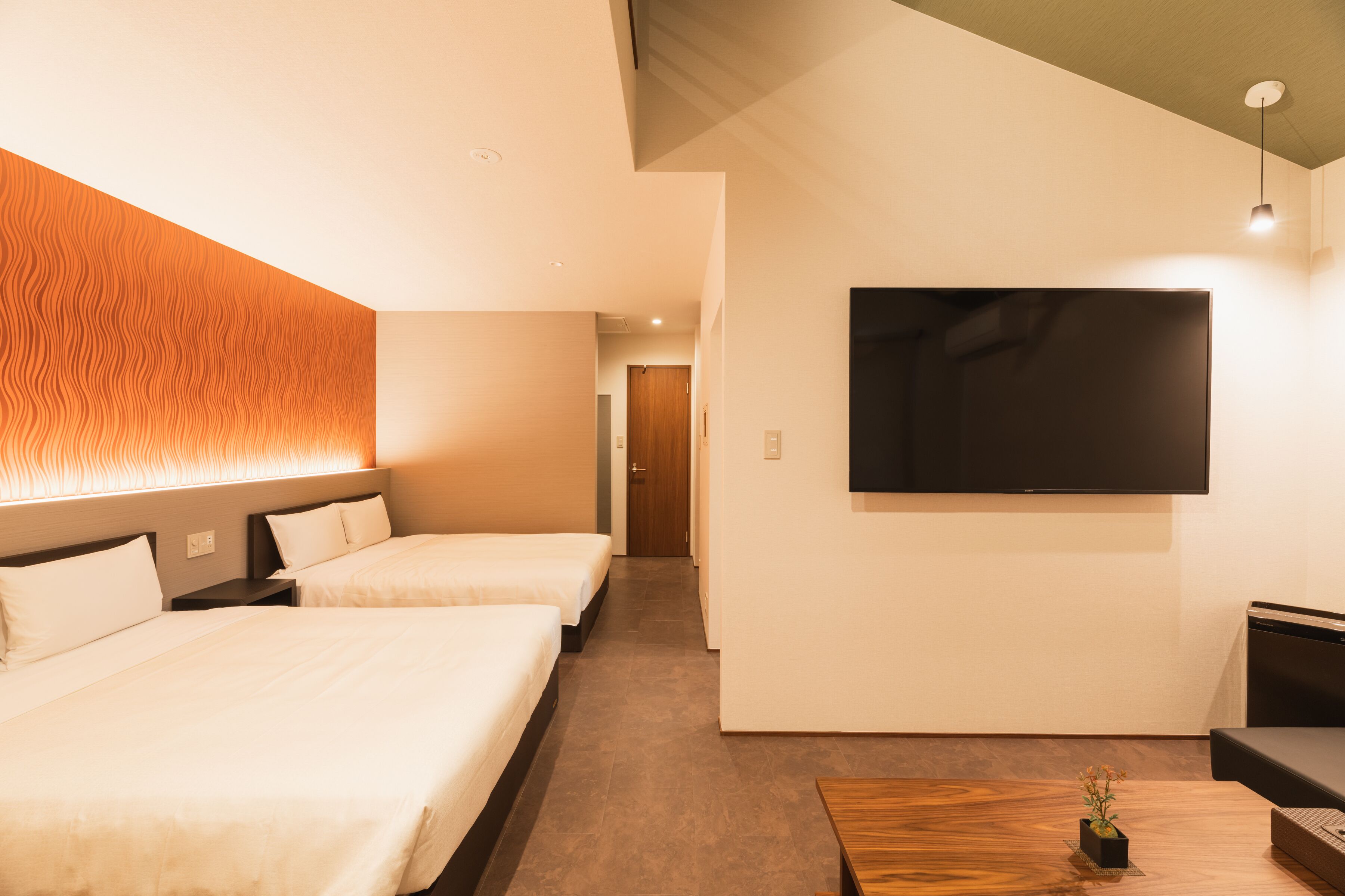 Une chambre d’hôtel avec deux lits, un téléviseur fixé au mur et une petite table agrémentée d’une plante.