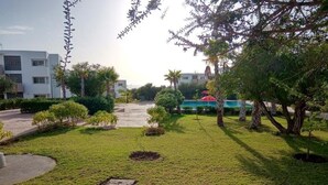 Un jardín bien cuidado con césped impecable, pequeños arbustos y árboles. Se observan varias tapas de alcantarilla en el césped.