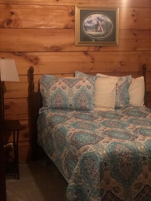 A wooden-paneled room with a bed, a nightstand, and a framed picture on the wall. -  2 bedroom 1 bath cabin      (Oneida)