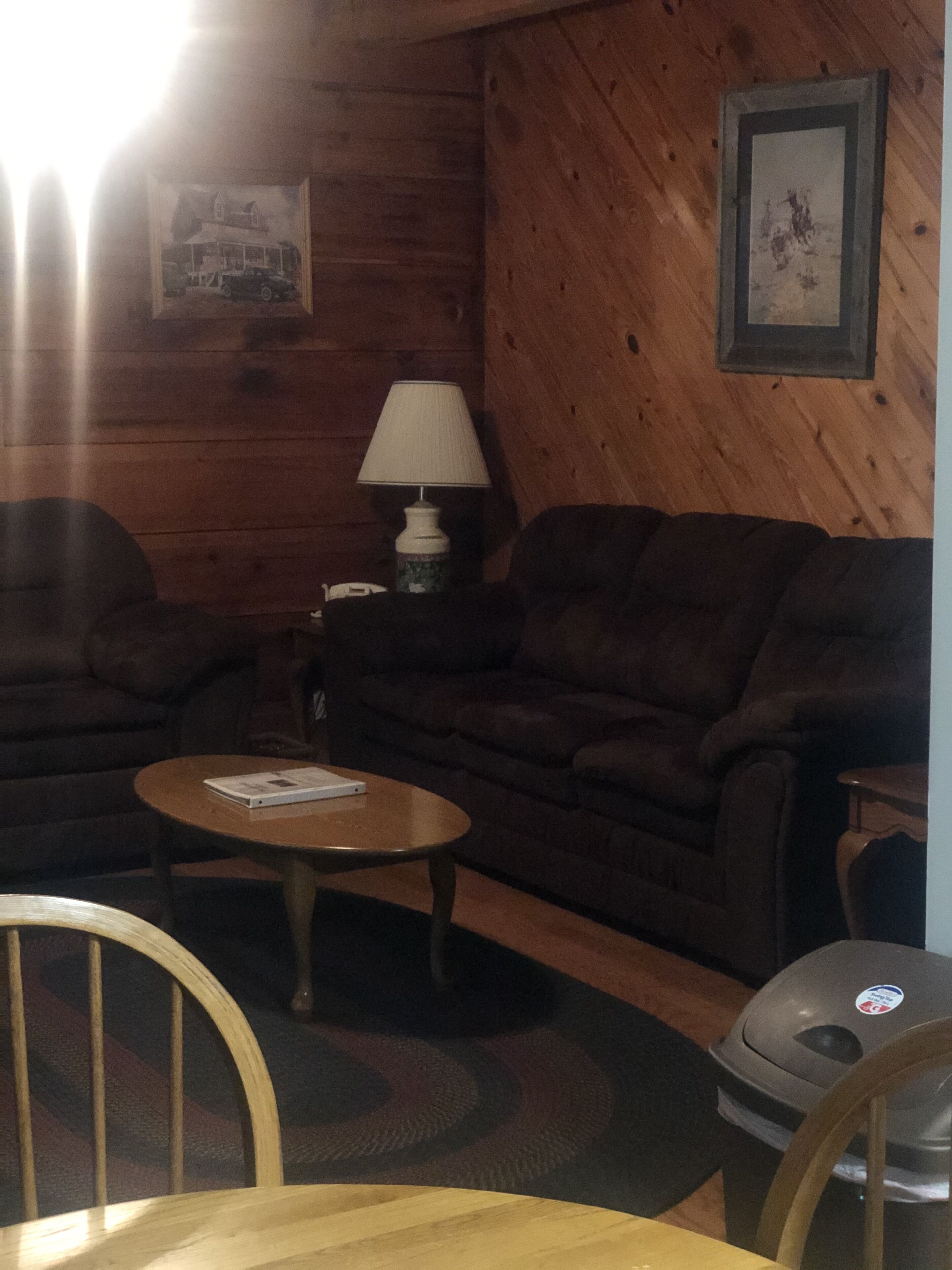 A cozy living room with a wooden wall, a sofa, a coffee table, a lamp, and a trash can.