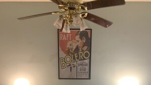Een slaapkamer met een bed, een plafondventilator, een poster aan de muur en twee wandlampen.