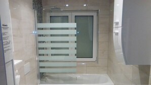 A bathroom with a bathtub, toilet, and a window with blinds.