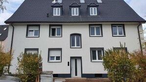 A two-story residential building with a dark tiled roof, multiple windows, and a front door.