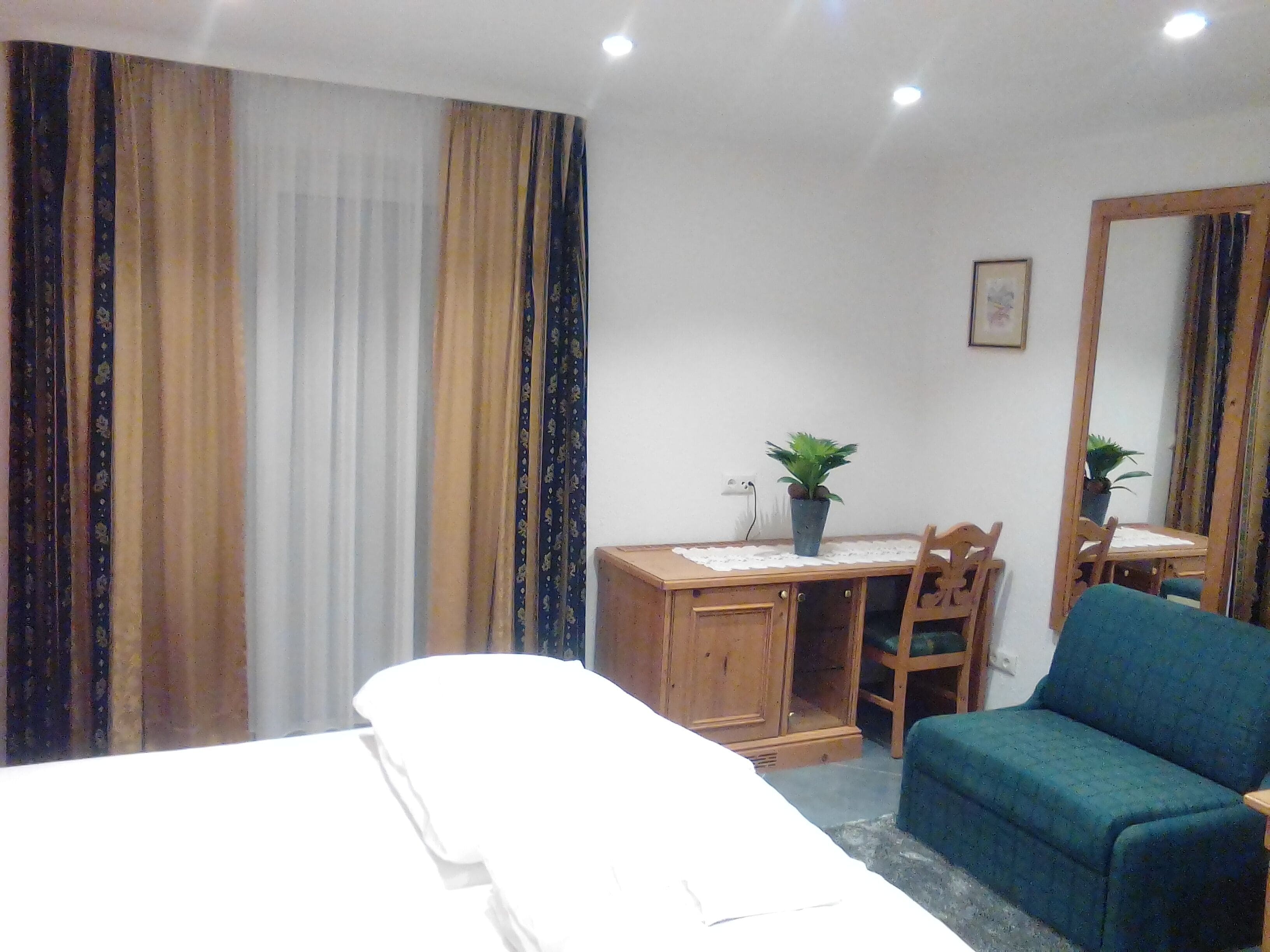 Habitación de hotel con cama, escritorio con silla, sillón azul y dos macetas.