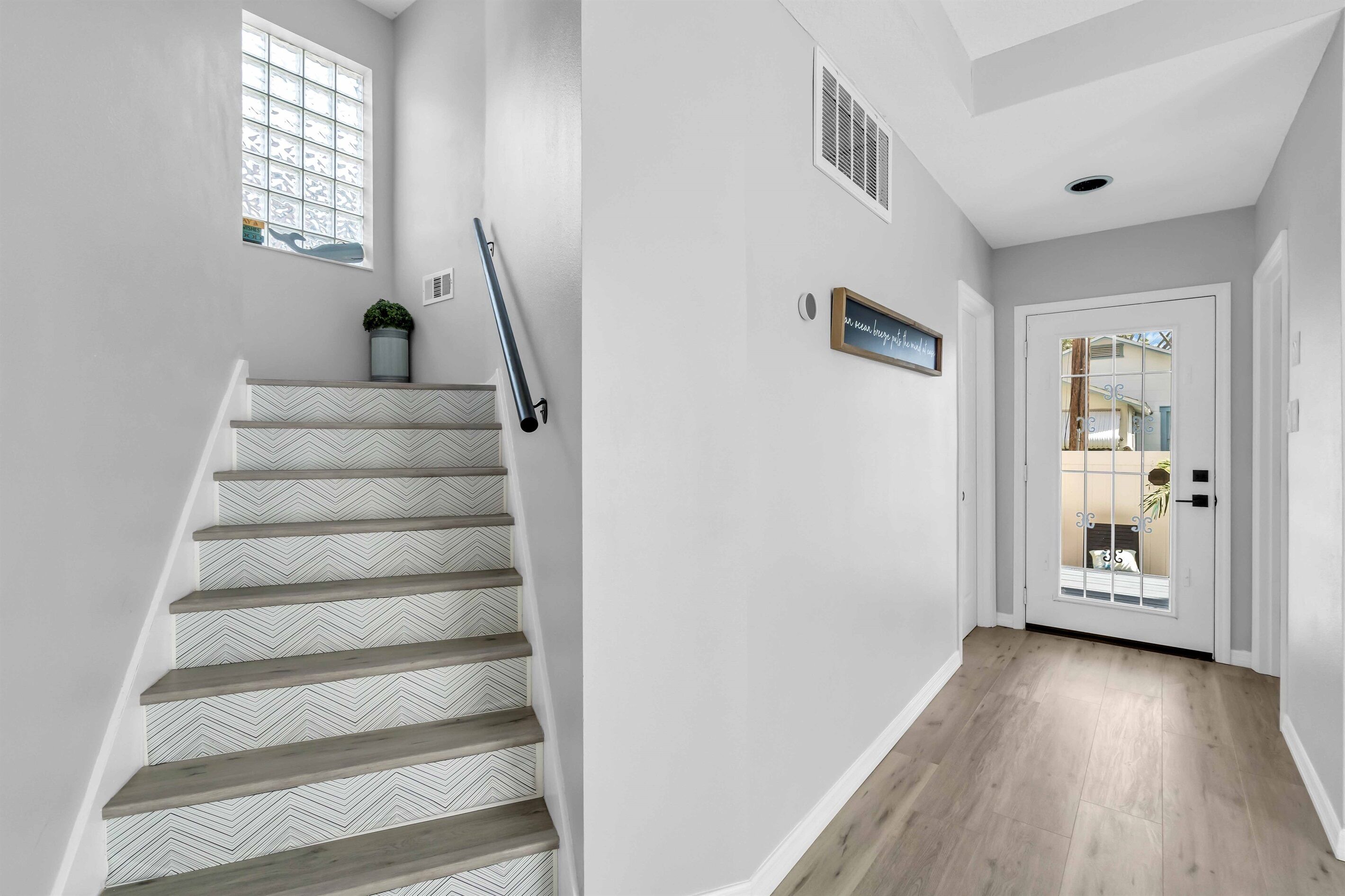 A staircase with a herringbone pattern, a potted plant, a wall-mounted sign, a door with a glass panel, and a vent.