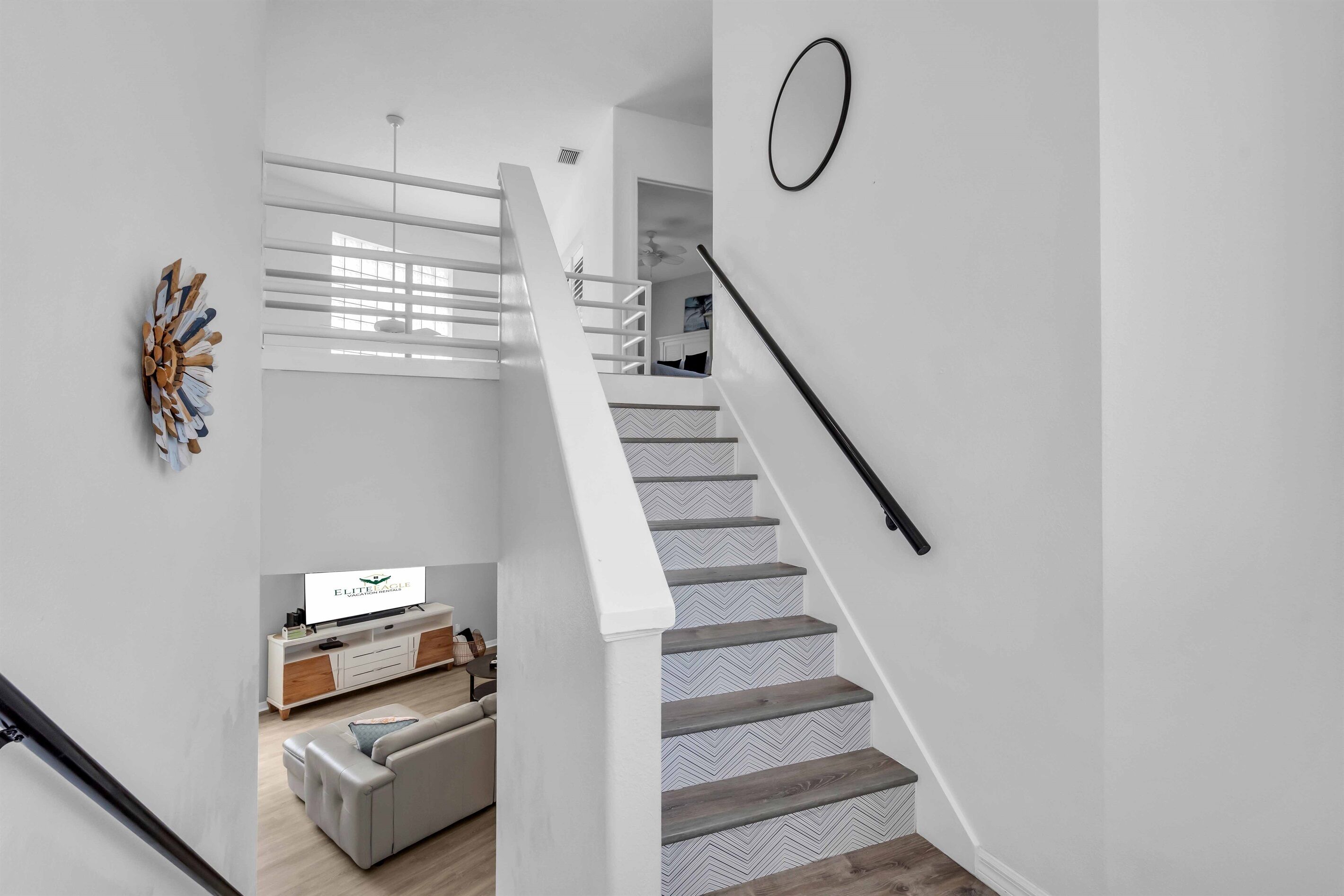 Un escalier au design moderne, un mur blanc orné d’un élément décoratif et un téléviseur diffusant une publicité pour « ELITE EAGLE Vacation Rentals ».