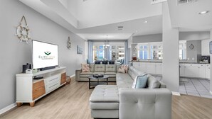 Un salon spacieux avec un grand canapé d’angle, un téléviseur à écran plat et une cuisine moderne en arrière-plan.