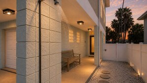 Un espace extérieur abrité, doté d’un banc, d’une porte et d’une clôture blanche.
