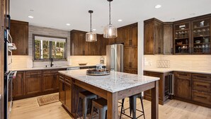 Une cuisine moderne avec des meubles en bois, un grand îlot central doté de tabourets, des appareils en acier inoxydable et un éclairage suspendu.