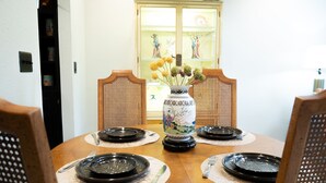 Een eettafel gedekt met zwarte borden, bestek en een decoratieve vaas met bloemen.