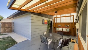 Een overdekte patio met een tafel, stoelen, een schommel en een houten omheining.