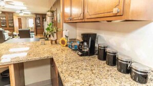 Una cocina con encimeras de granito, armarios de madera, cafetera y una planta colgante.