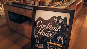 Un cartel en marco que anuncia 'Cocktail Hour' con detalles del menú de bebidas y horario de apertura.
