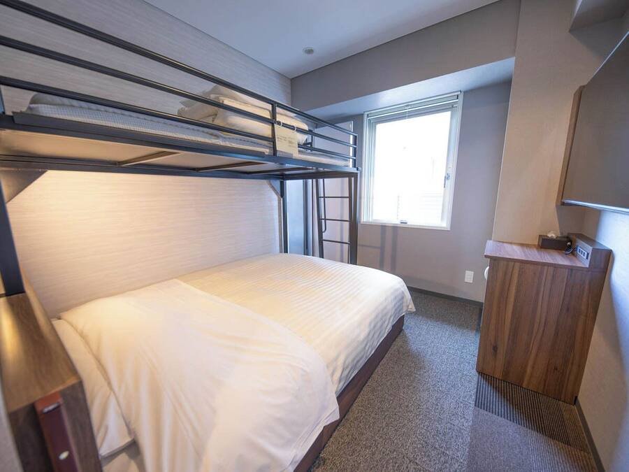 A bunk bed room with a window, a desk, and a mirror.