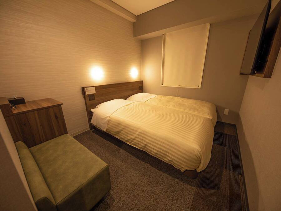 A hotel room with a bed, a bedside table, a chair, and a window.