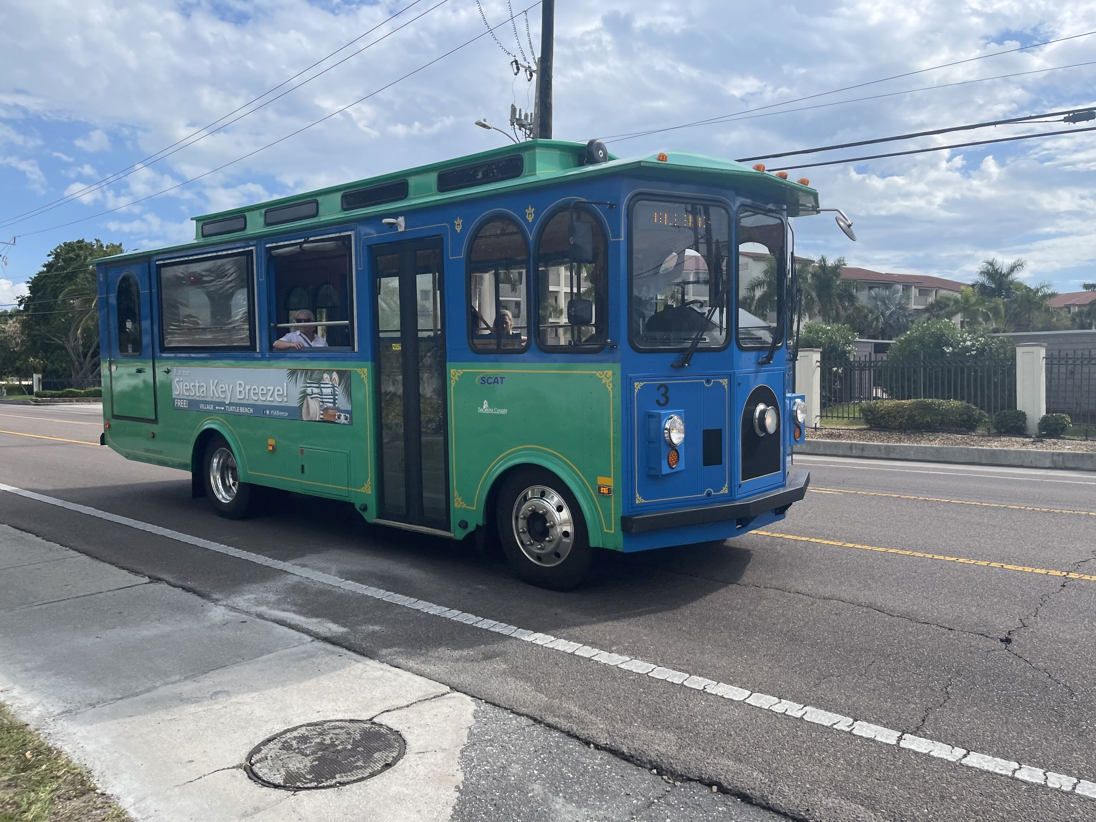 Un autobus bleu et vert, orné de publicités sur ses flancs, circule sur une route.