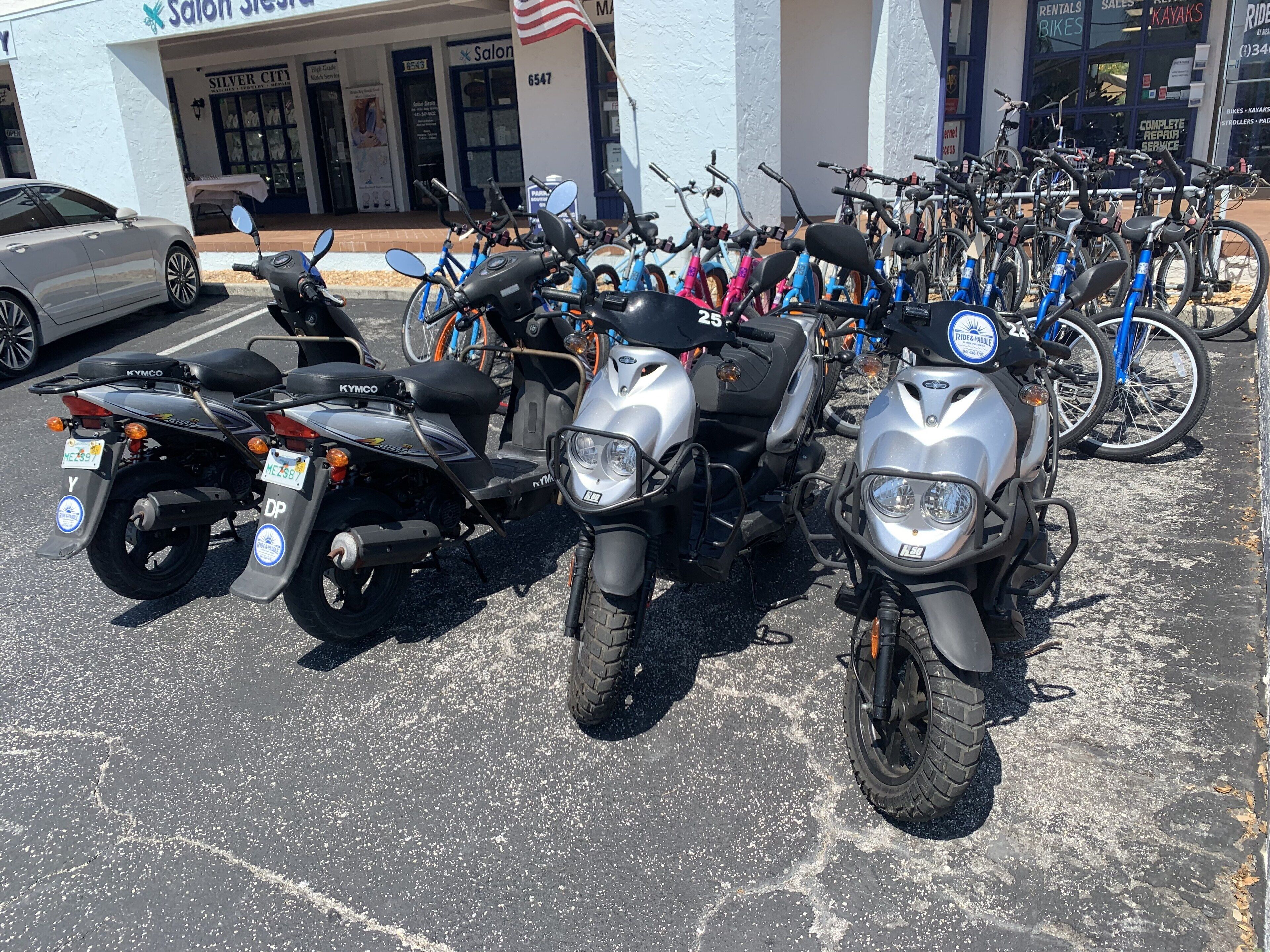 A row of motorcycles parked in front of a building with signage for a salon and a kayak rental service.