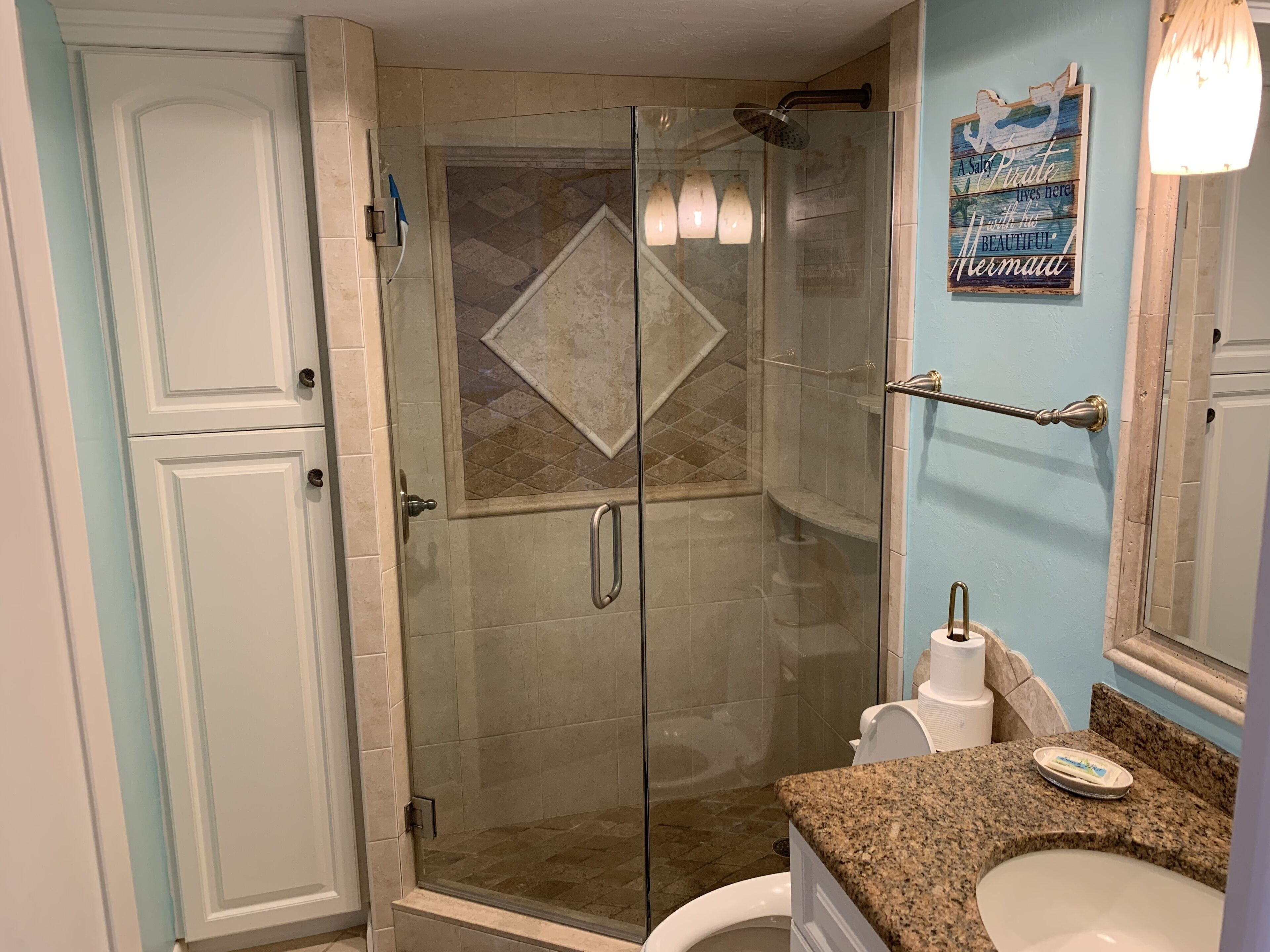 A bathroom with a glass-enclosed shower, a toilet, and a sink with a granite countertop.