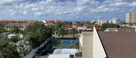 A residential area with a tennis court, palm trees, and buildings with red roofs.