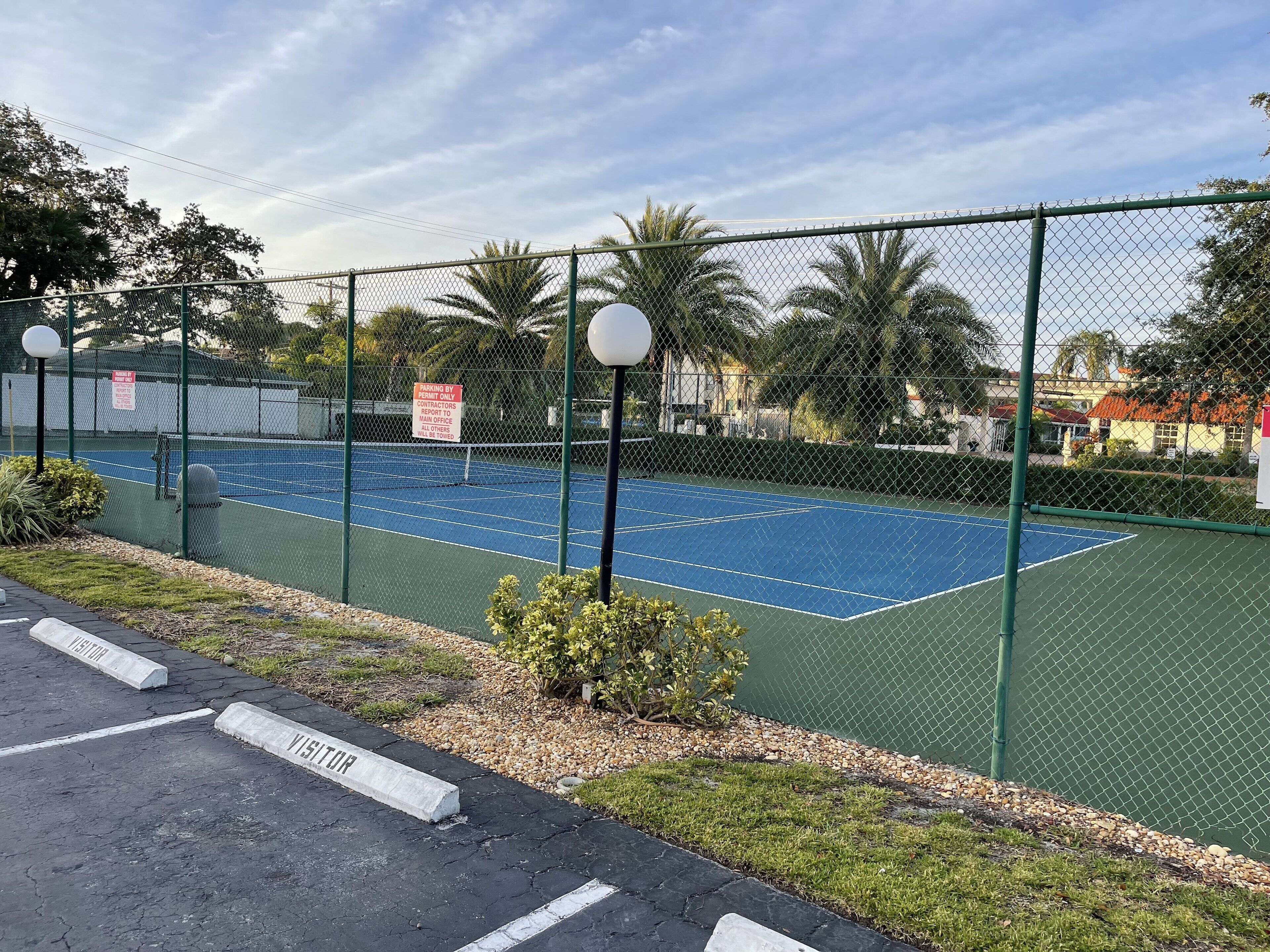A tennis court enclosed by a chain-link fence with a sign indicating parking by permit holders only.