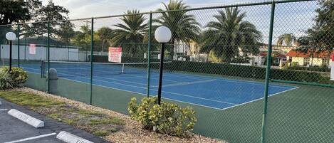 A tennis court enclosed by a chain-link fence with a sign indicating parking by permit holders only.