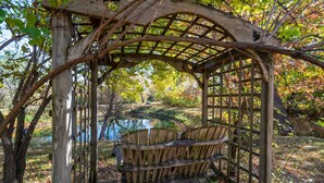 A wooden gazebo with a bench, surrounded by trees and a pond. -  AMAZING & A PARTY BARN… HOT TUB, PL TBl, PNG PNG, & ARCADE!  ACCESS TO POOLS! (West Des Moines)