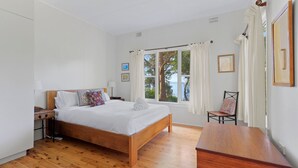 Una camera da letto con un letto in legno, un comodino, una sedia, un tavolo in legno e una finestra vista alberi e acqua.