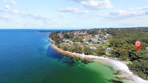 Una vista aerea di una località costiera con spiaggia, case e una fitta foresta.