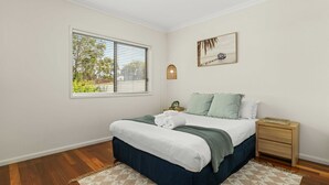 Quarto com cama, mesa de cabeceira, lumin ária na parede e janela com persianas.