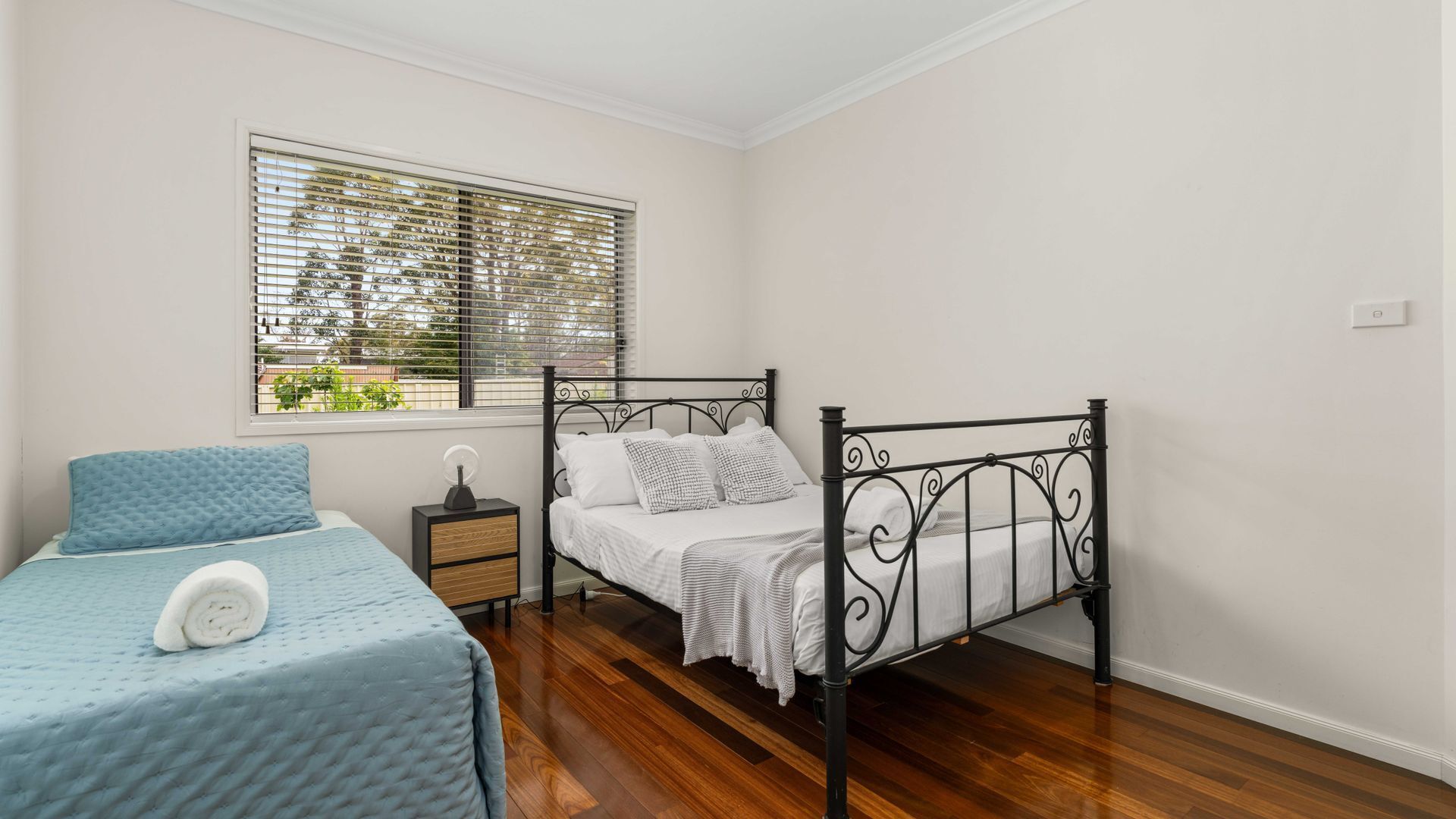 A bedroom with a single bed, a bedside table, and a window with blinds.
