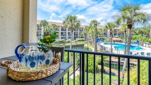 A balcony with a view of a swimming pool, palm trees, and a building with balconies. - Views, Two Pools, Brand New Bathrooms, Updated Furniture, Direct Beach Access! $300 in Free Tickets! (St. Augustine Beach)