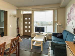 A living room with a sofa, a table, a TV, and a window with blinds. - Hiihtäjäntie 1 as 3 by Interhome (Ylläsjärvi)