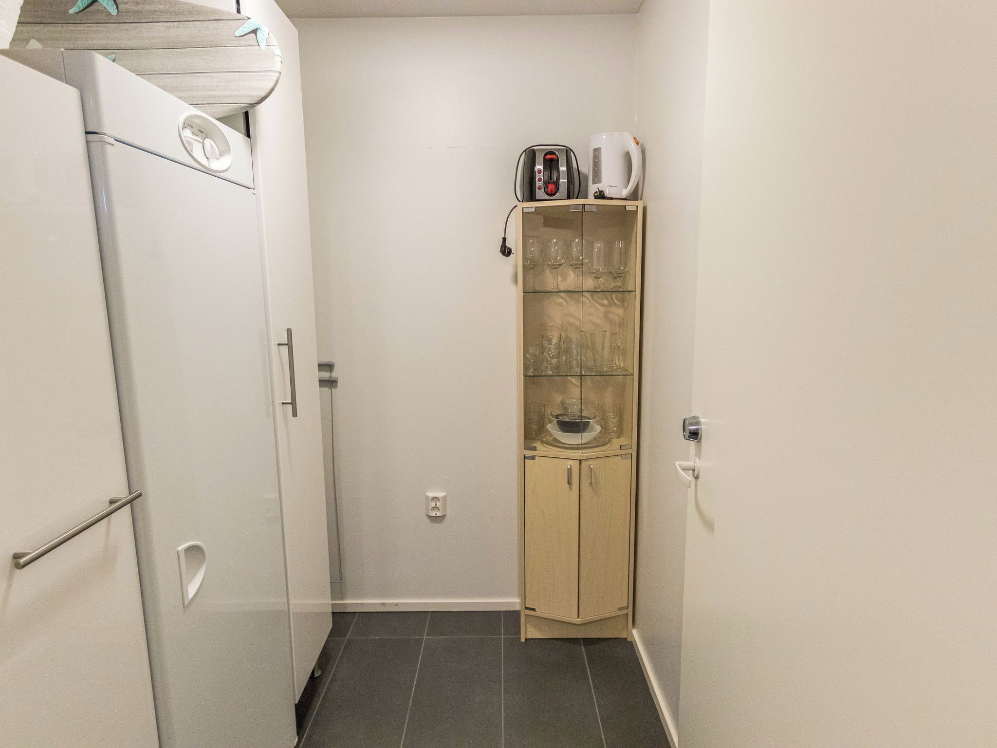 A compact kitchen with a refrigerator, a microwave, a coffee maker, and a glass cabinet with wine glasses.