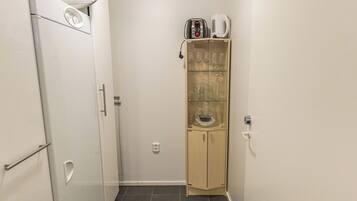 A compact kitchen with a refrigerator, a microwave, a coffee maker, and a glass cabinet with wine glasses.