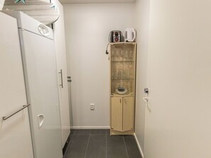 Une cuisine compacte équipée d’un réfrigérateur, d’un four à micro-ondes, d’une machine à café et d’une vitrine contenant des verres à vin.