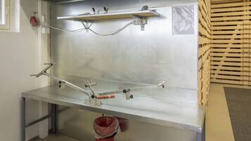 A stainless steel workbench with a metal shelf above and a red trash bin underneath.