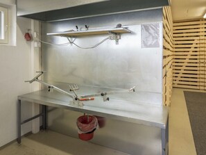 Un établi en acier inoxydable, avec une étagère en métal au-dessus et une poubelle rouge en dessous.