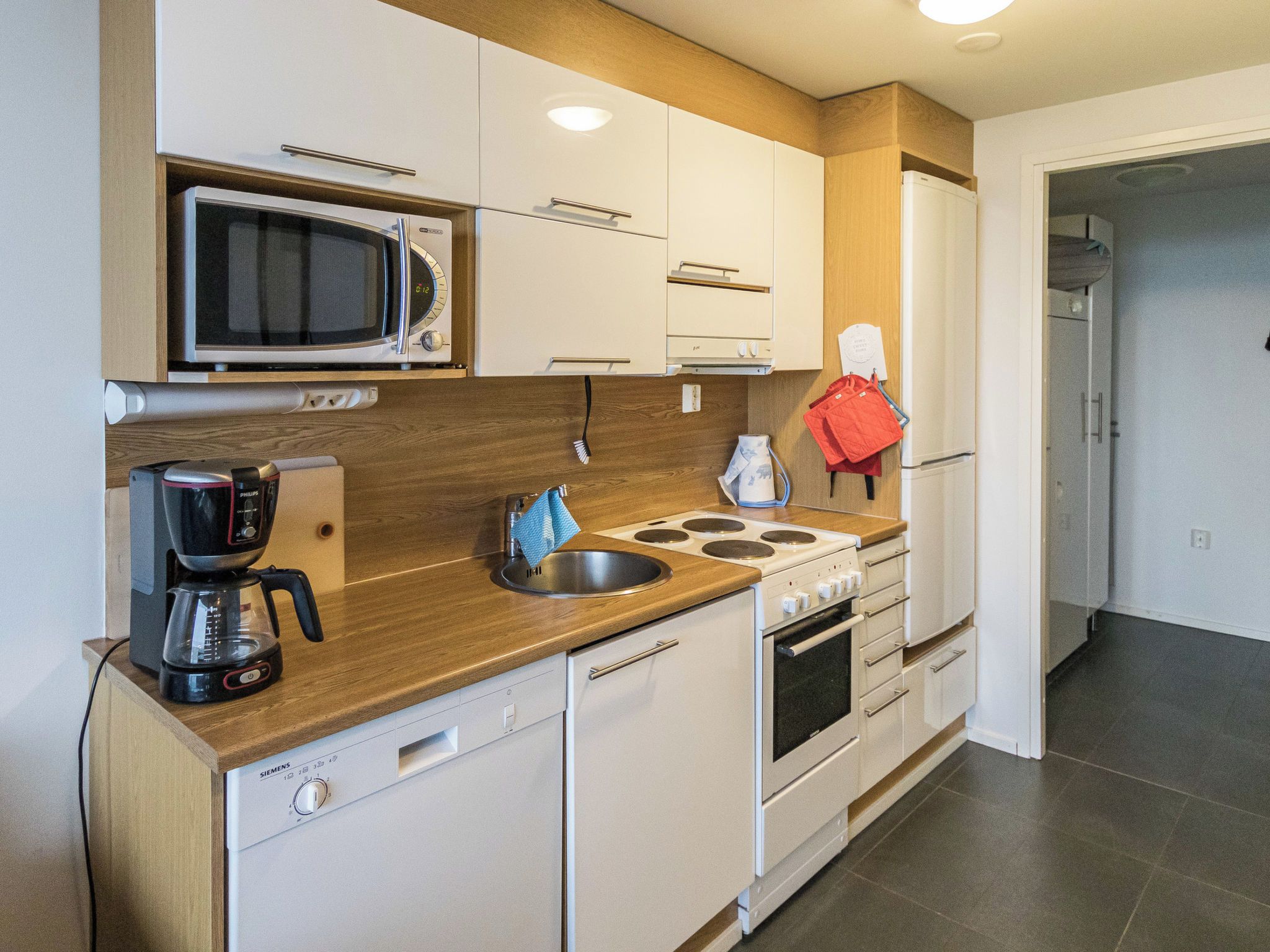 A compact kitchen with a microwave, coffee maker, sink, stove, and cabinets.