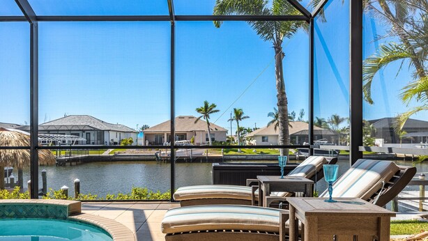 A poolside area with lounge chairs and a view of a body of water and houses in the background.