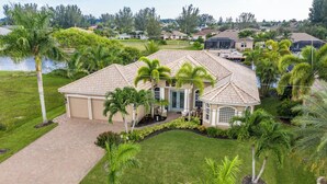 A single-story house with a tiled roof, surrounded by a well-maintained lawn and palm trees.