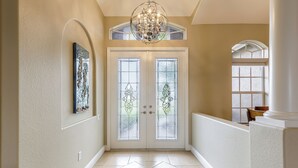 A hallway with a double door, a chandelier, and a tiled floor.
