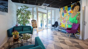 Un vestíbul modern amb sofàs color turquesa, una taula de centre i un mural gran, i una porta de vidre que dona a l'exterior.